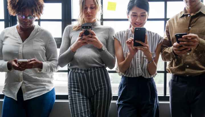 three women standing near man holding smartphones