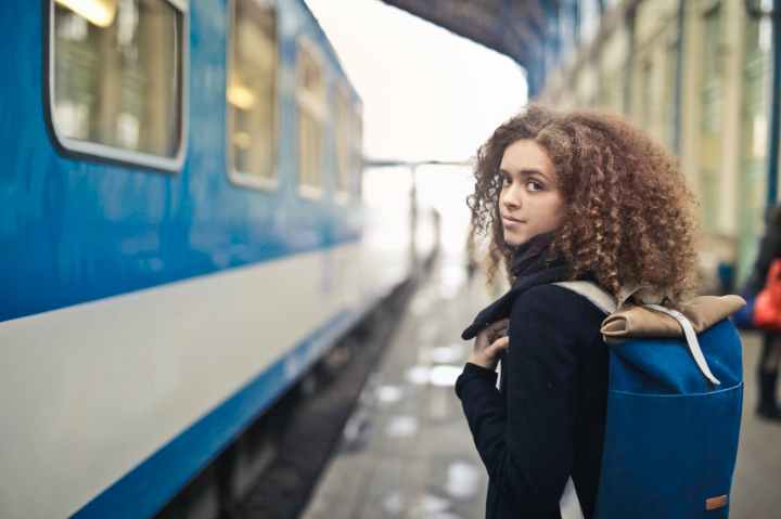 woman in black coat standing beside blue and white train