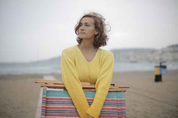 calm female tourist with folded deckchair standing alone on seashore in overcast weather
